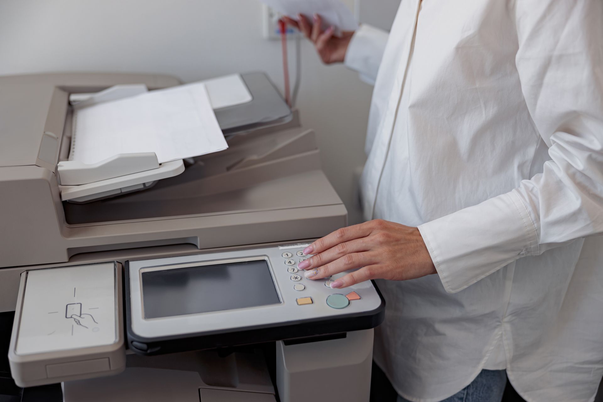 A woman is using a copier to copy a piece of paper.