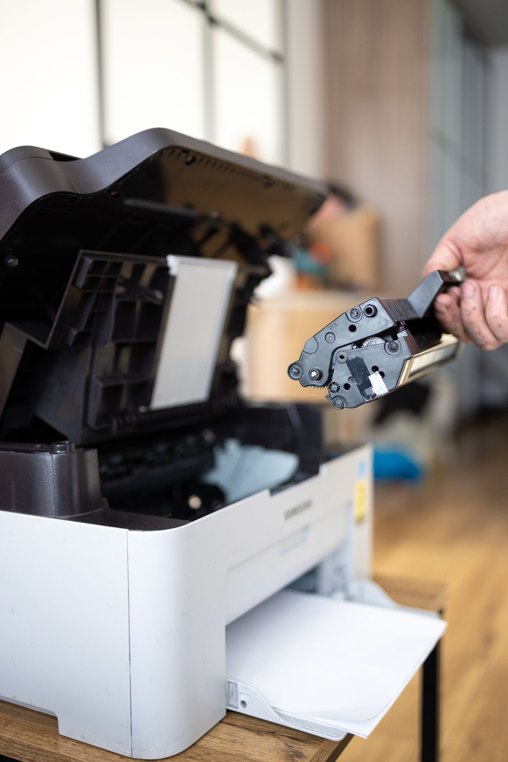A person is holding a cartridge in front of a printer.