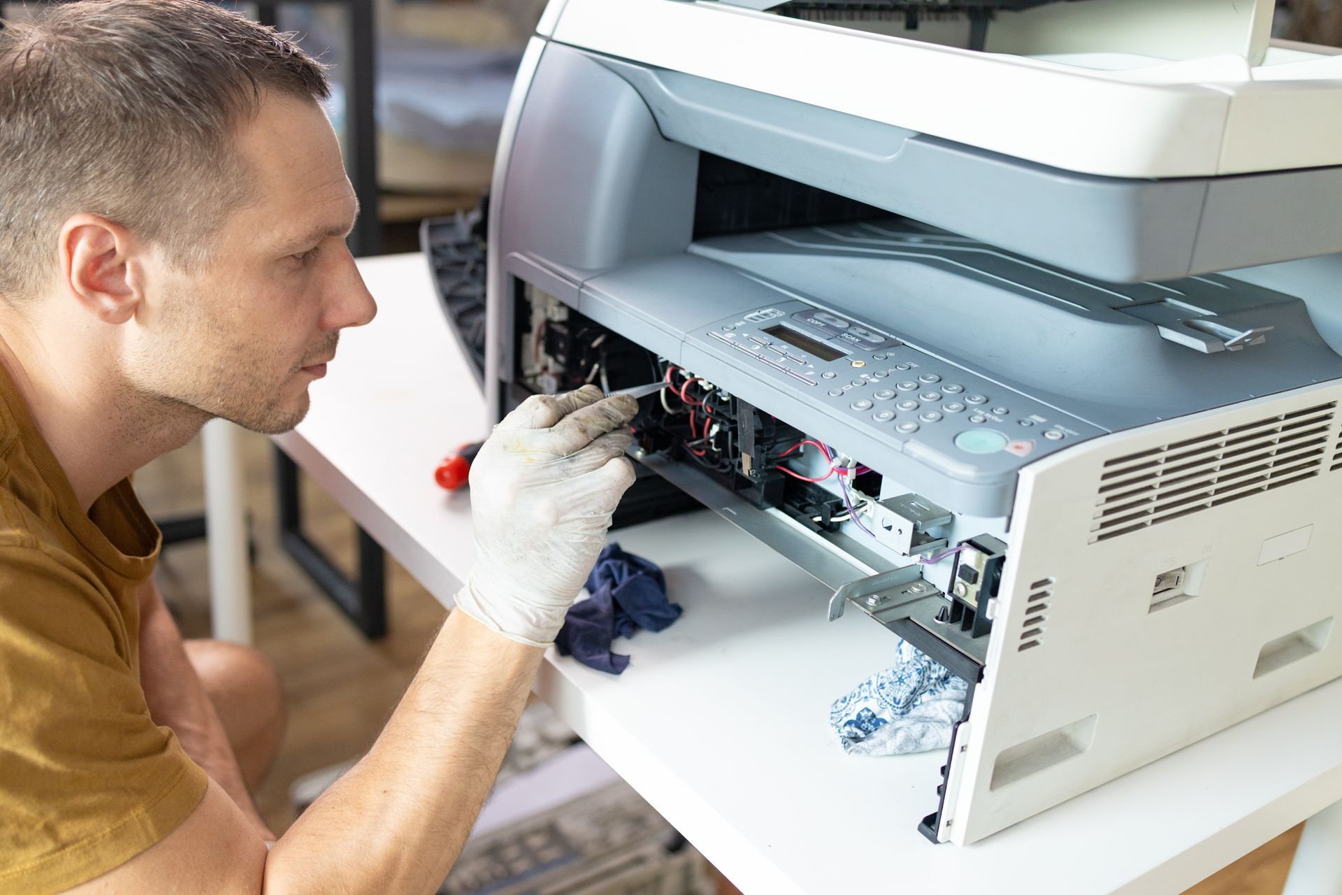 A man is fixing a printer on a desk.