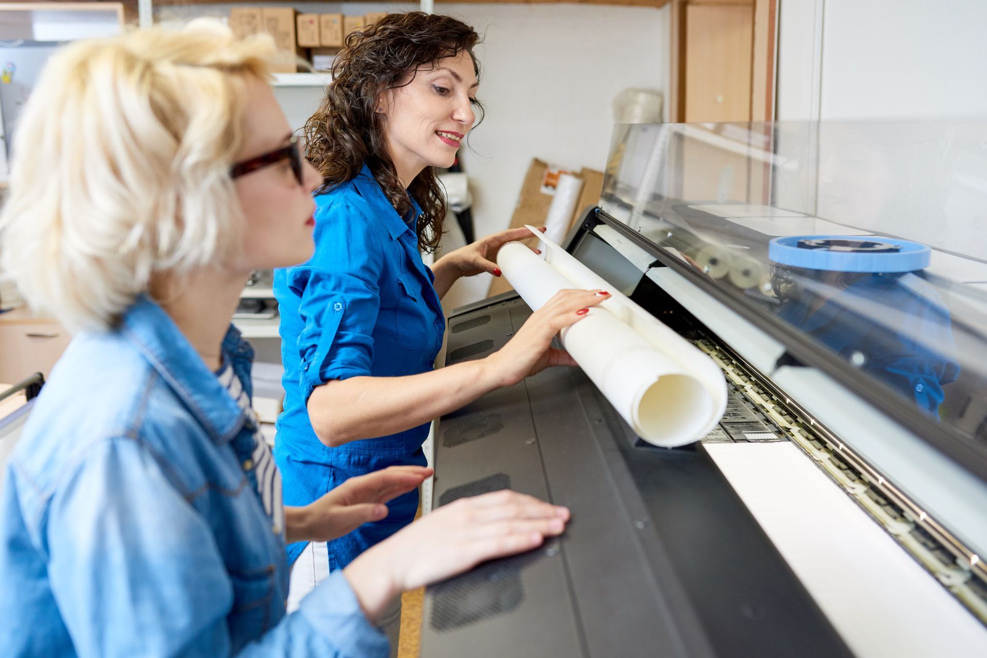 Two women are working on a large printer in a factory.