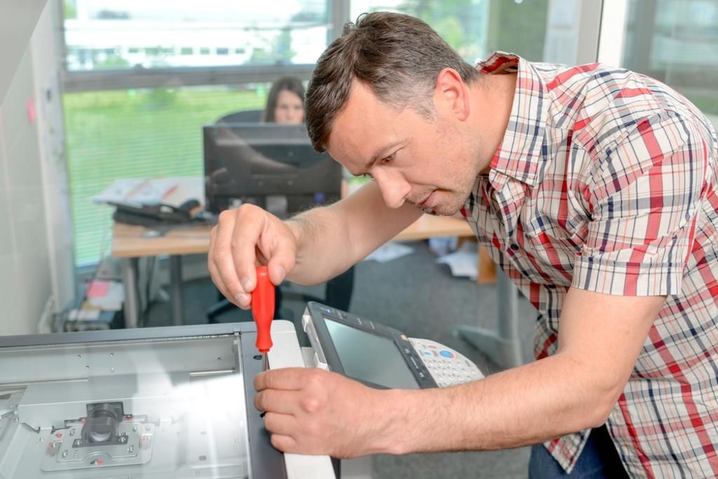 A man is fixing a printer with a screwdriver.