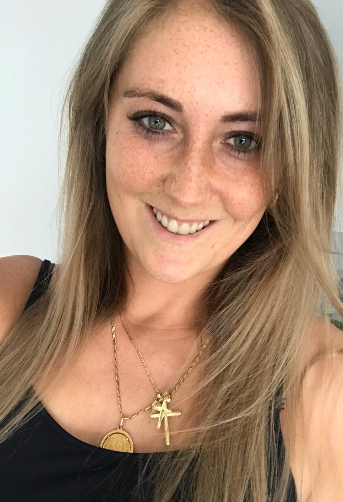 Eine Frau in einem schwarzen Tanktop und einer goldenen Halskette lächelt in die Kamera.