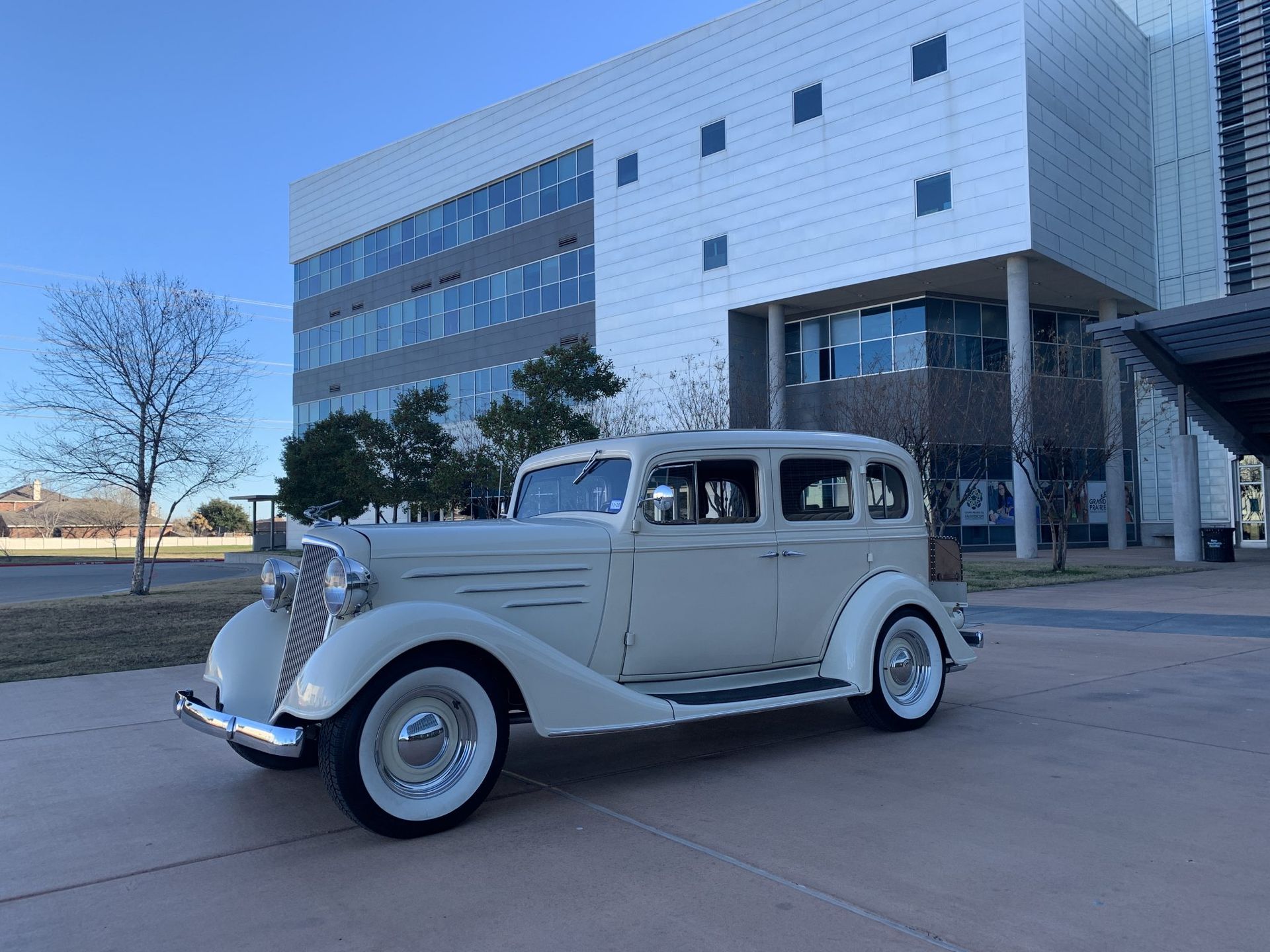 An old white car is parked in front of a building.