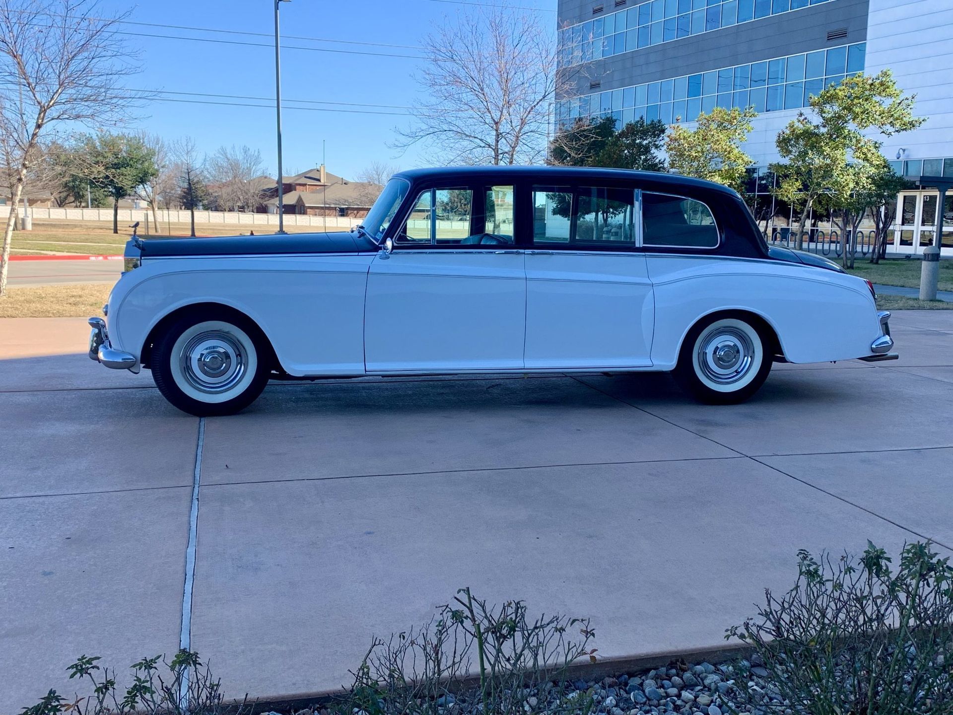 A white car is parked in a parking lot in front of a building.