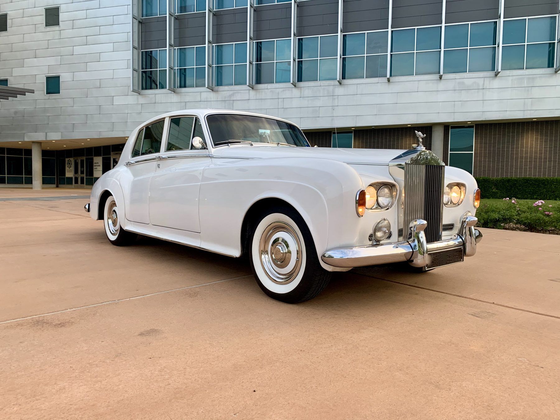 A white rolls royce is parked in front of a building.