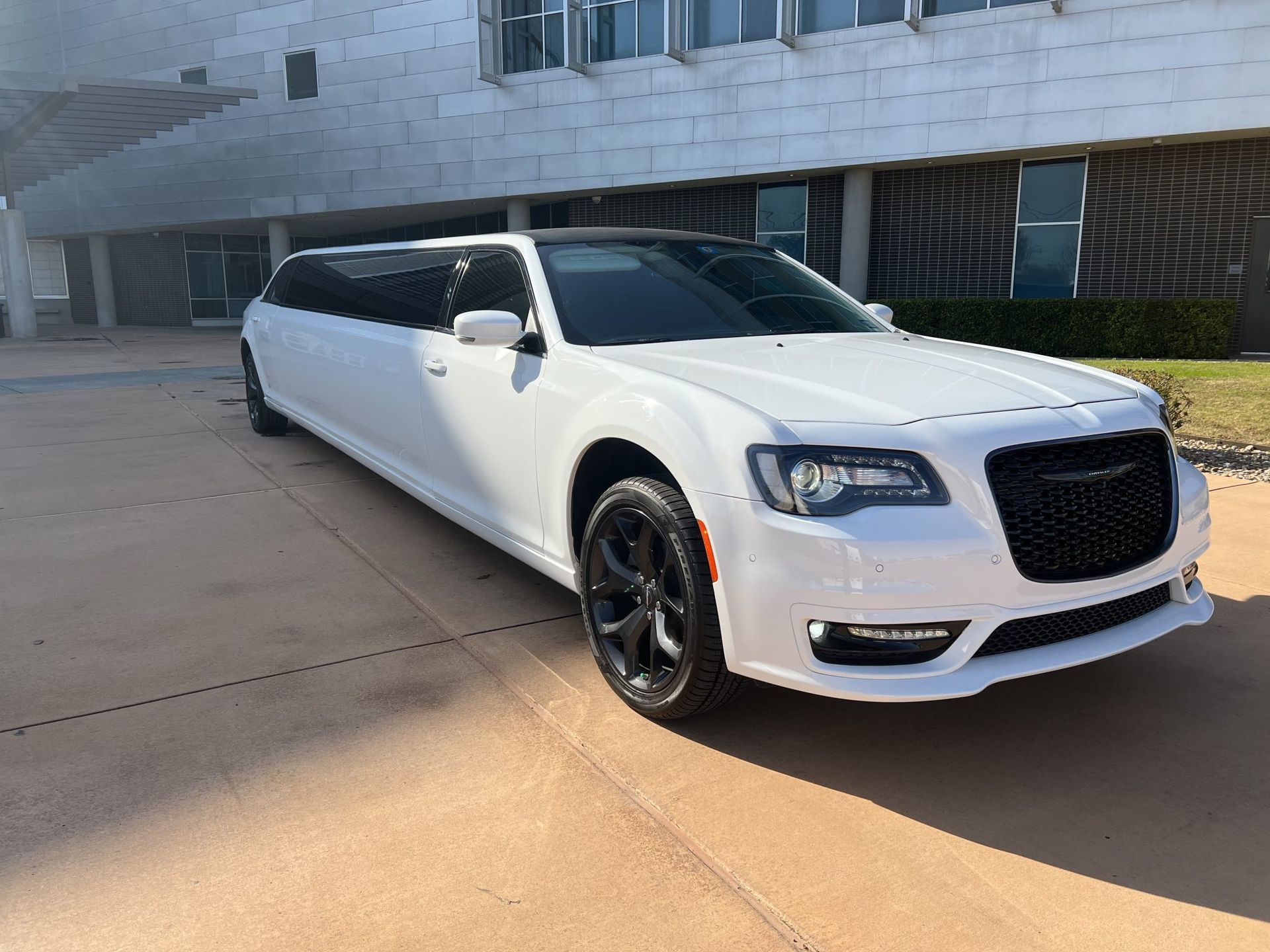 A white limousine is parked in front of a building.