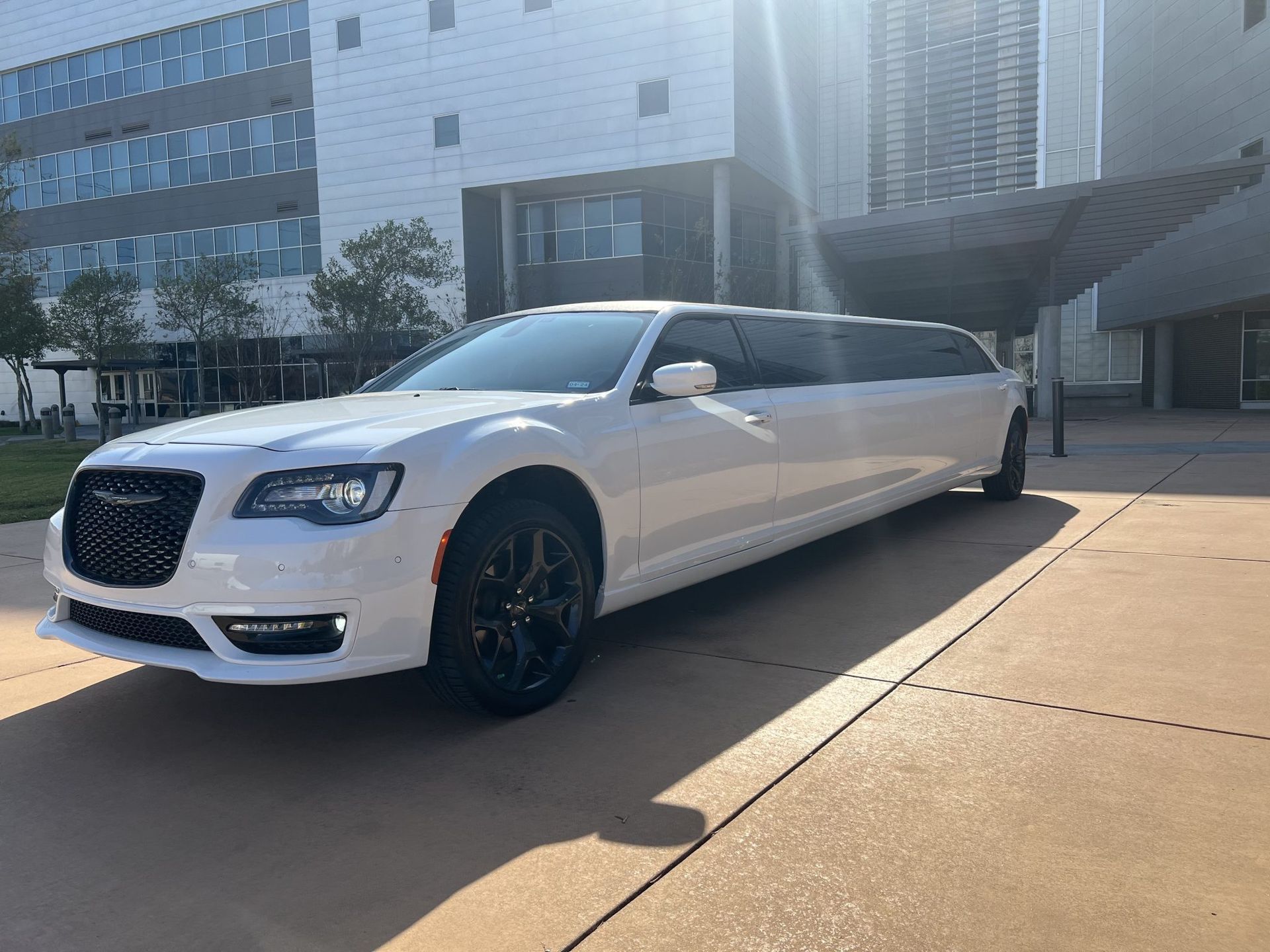 A white limousine is parked in front of a building.