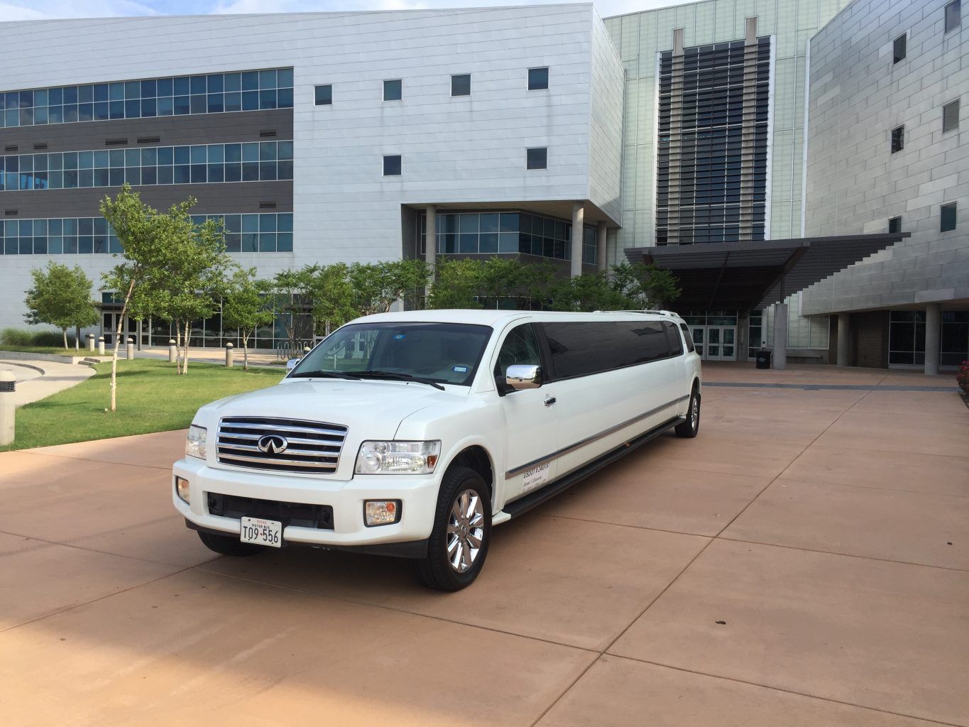 A white limousine is parked in front of a large building.