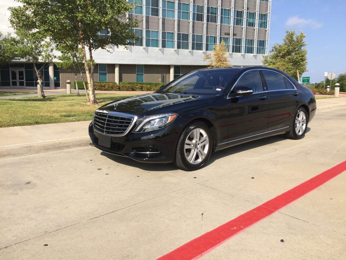 A black mercedes benz s class is parked in a parking lot in front of a building.