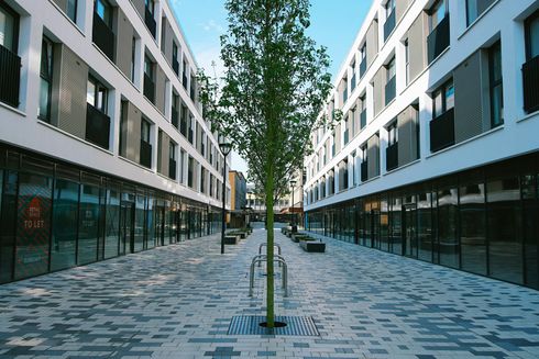 Row of modern white buildings with shops, a tree in the center of a paved walkway.