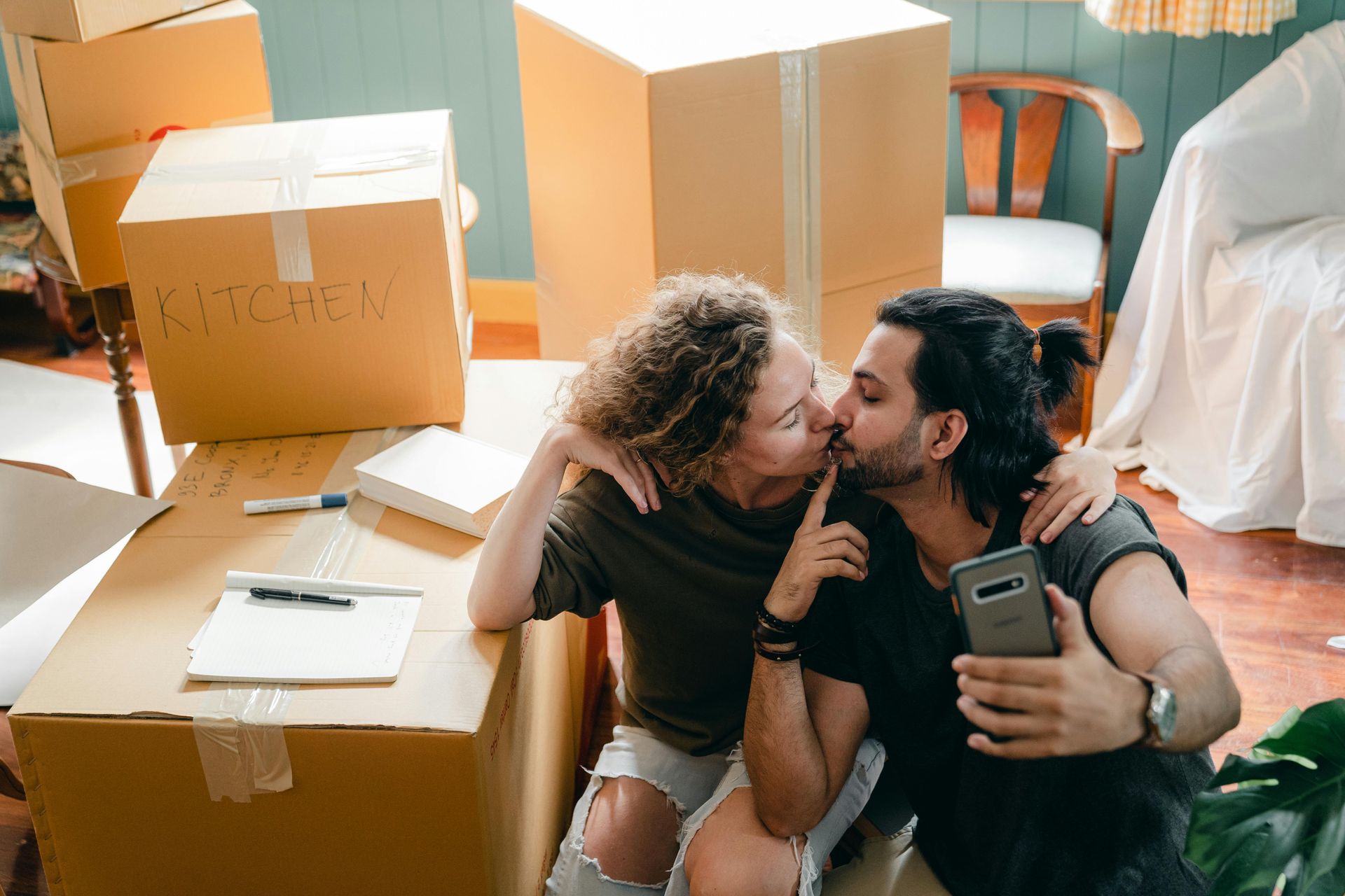 Couple taking a selfie while moving, surrounded by cardboard boxes.