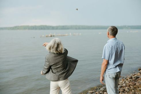 Woman throwing a rock into a lake while a man watches. They stand on a rocky shore.