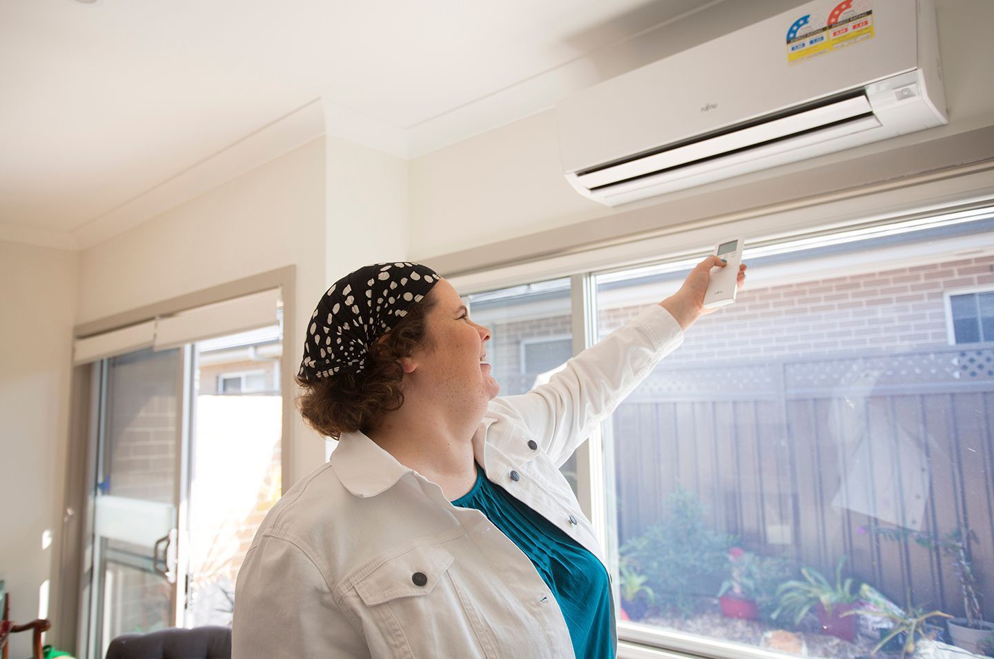 A Woman Is Adjusting The Temperature Of An Air Conditioner — Marty Nelson Refrigeration & Air Conditioning In Dubbo, NSW