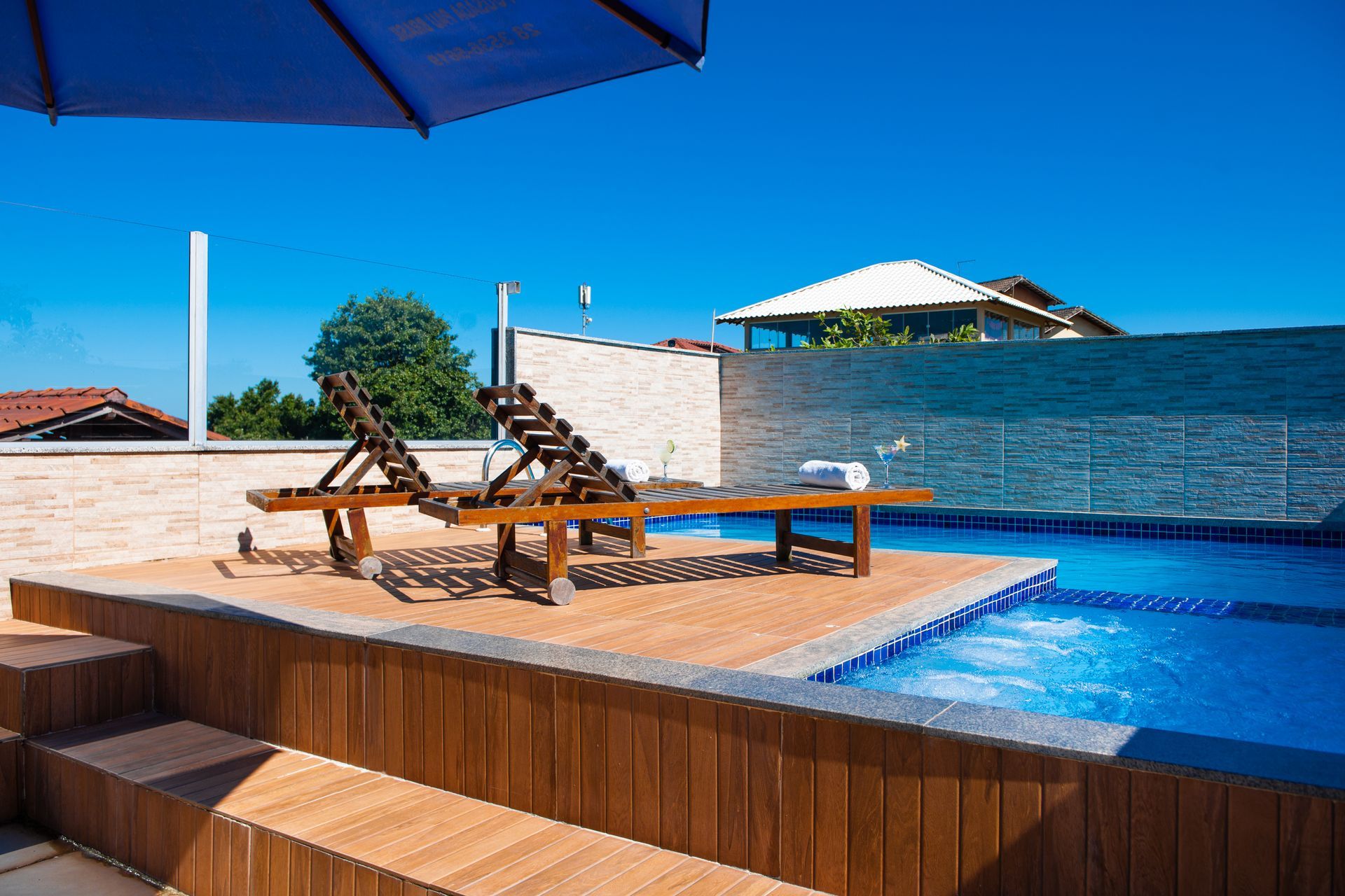 Uma piscina com espreguiçadeiras de madeira e um guarda-sol azul. Pousada Pau Brasil