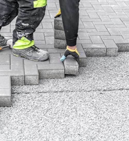 A person is laying bricks on a sidewalk.