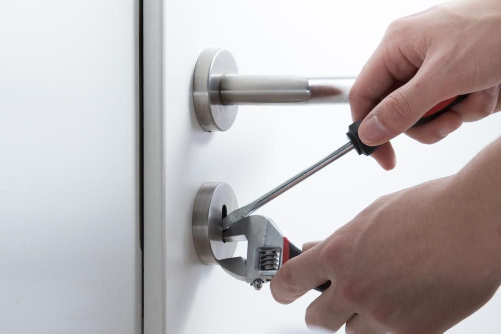 A Person Is Fixing a Door with A Wrench and Screwdriver — Tropical Locksmiths in Gregory River, QLD