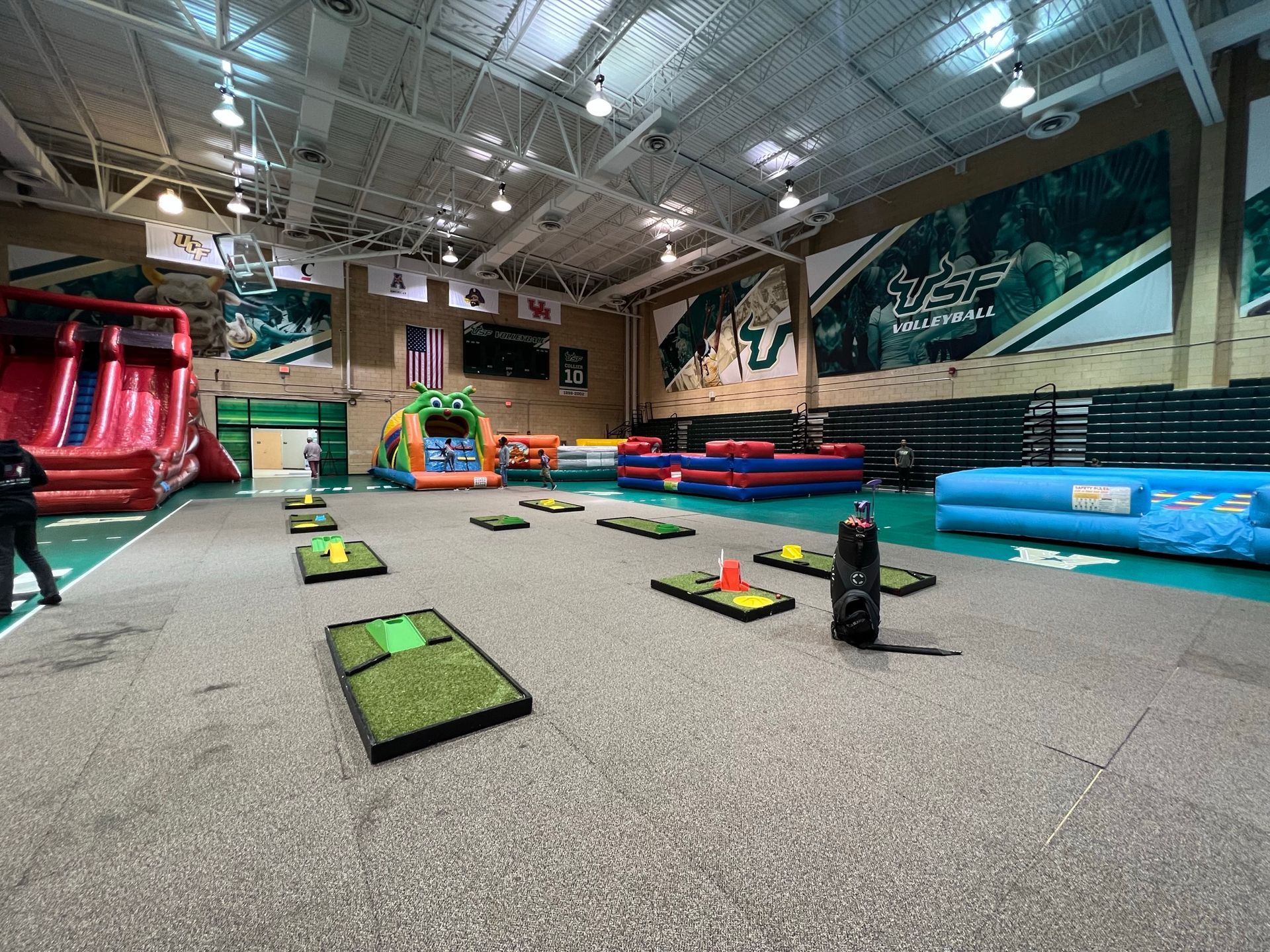 A gymnasium transformed into a fun zone with a portable mini golf course and inflatable slides, 