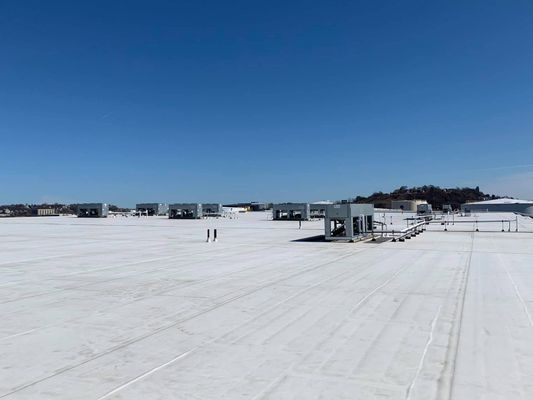 A vast, white commercial flat roof stretching toward the horizon with several small grey vent hoods installed across the surface.