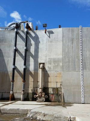 Three black pipes secured to a light-colored concrete wall with a measurement ruler on the side.