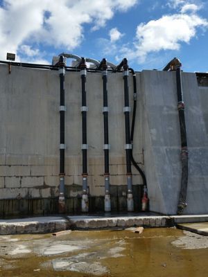 Five black industrial pipes running vertically down a concrete structure near water.