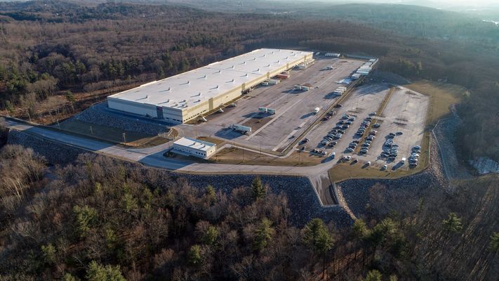 A high-angle view of a large distribution center with a truck yard and parking lot.
