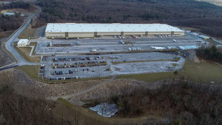 A large industrial water reservoir with floating liners and a massive warehouse in the background.