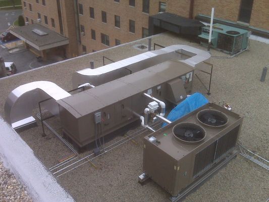 A wide view of rooftop HVAC equipment, including a large condenser unit with dual fans and connected ducting.