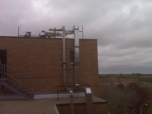 Vertical silver exhaust stacks and industrial venting mounted to the exterior wall of a brick building.