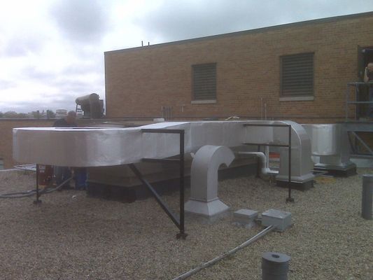 Large silver-insulated rectangular ductwork and an elbow vent installed on a gravel-topped commercial rooftop.