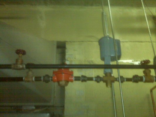 Close-up of an orange industrial valve and black piping system with a pressure gauge installed in a mechanical facility.