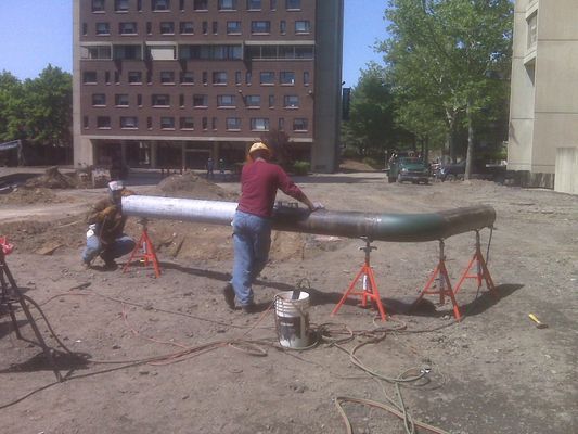 Workers on-site preparing a large elbow-joint pipe section supported by red jacks for installation.