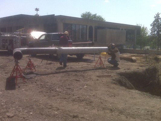 A long section of silver industrial piping supported by red metal stands on a dirt construction lot.