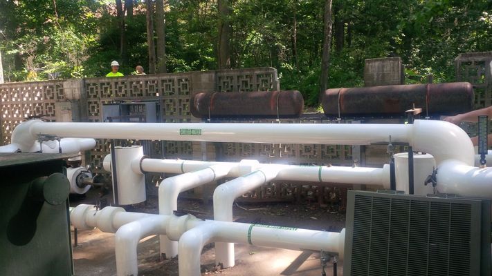 White PVC or painted pipes with elbow joints and valves in an outdoor facility.