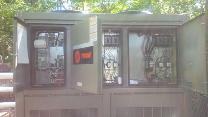 An open electrical control panel on a Trane HVAC unit, showing internal circuit breakers and wiring components.