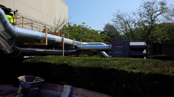 Large insulated silver HVAC pipes running horizontally along the exterior of a commercial building.