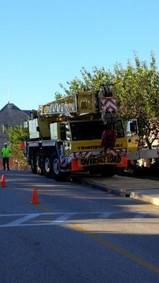 A large multi-axle mobile crane parked on a street with orange safety cones, labeled with an 