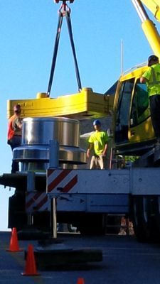 Workers on a flatbed truck preparing a large, circular metallic HVAC exhaust fan for lifting.