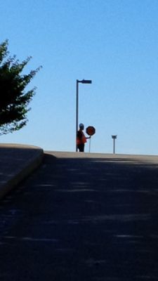 A safety flagger in a high-visibility vest standing on a road to direct traffic near a construction zone.