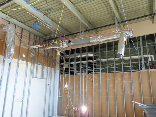 Interior view of a building under construction featuring exposed steel wall studs and overhead silver-insulated ductwork.