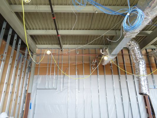 A perspective shot of the ceiling structure during construction, showing electrical wiring and metal ducting against a corrugated steel roof deck.