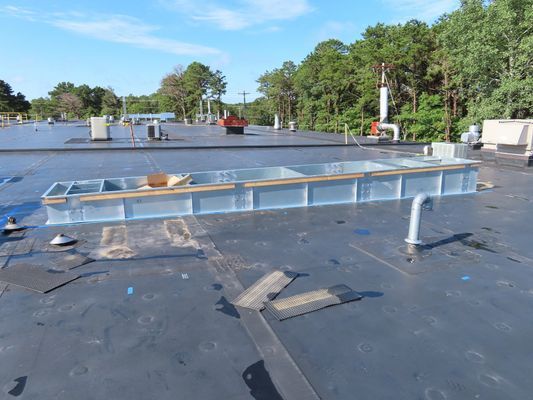 A wide view of a large, black flat rooftop featuring installed metal curbing and various drainage or utility connections.