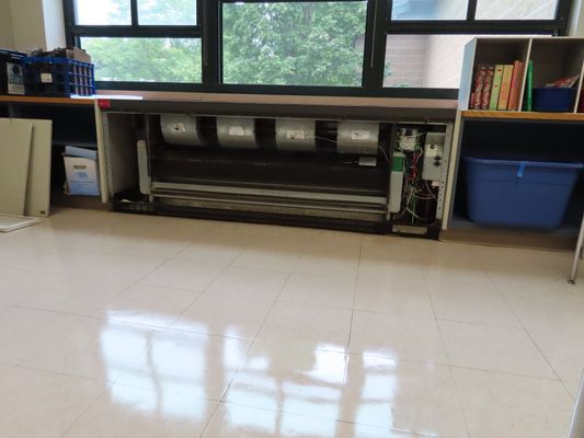 Interior view of an open floor-mounted HVAC unit cabinet located beneath a window in a commercial or institutional room.