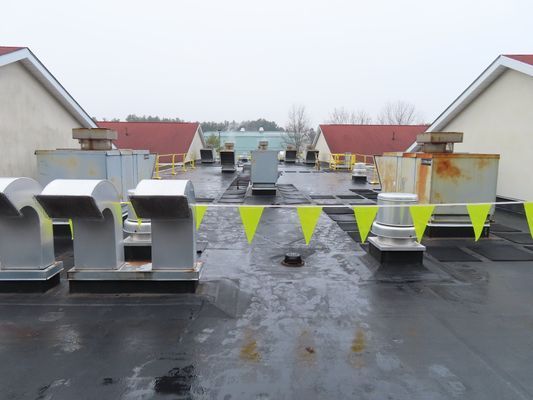 A flat commercial rooftop under a grey sky, featuring several small exhaust vents and yellow safety flags.