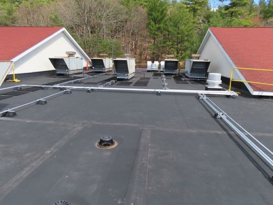 A wide rooftop view featuring several white commercial HVAC units and metal conduits running across a black flat roof.