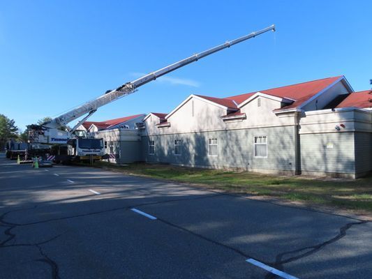 A perspective shot from the street looking up at a crane boom reaching over the roof of a grey building.