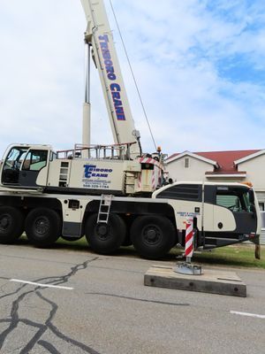 A large white mobile crane parked on a street with its stabilizers deployed, preparing for a heavy lifting operation.