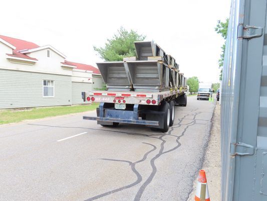 A flatbed truck carrying large metal HVAC components down a suburban road for delivery to a job site.