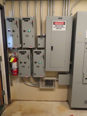 A wall-mounted array of multiple electrical boxes and a red fire extinguisher in a commercial facility.