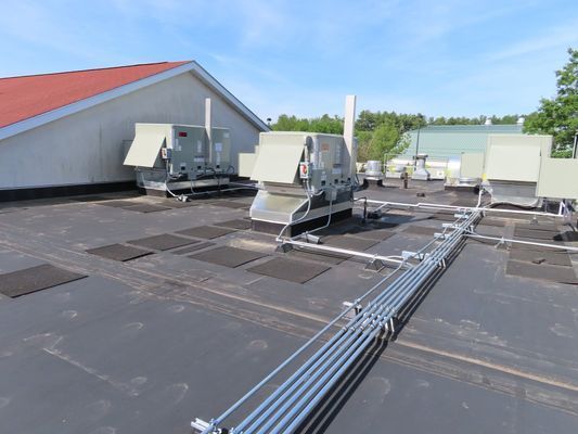 Several large silver mechanical units and conduit lines installed on a flat industrial roof.