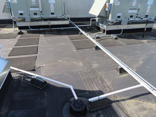 White PVC drainage pipes intersecting on a commercial roof surface.